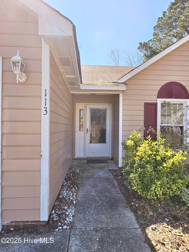 view of exterior entry featuring a shingled roof