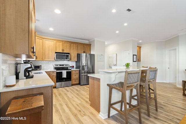 kitchen featuring visible vents, decorative backsplash, a breakfast bar area, ornamental molding, and stainless steel appliances