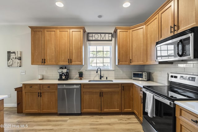 kitchen featuring stainless steel appliances, a sink, light countertops, backsplash, and light wood finished floors