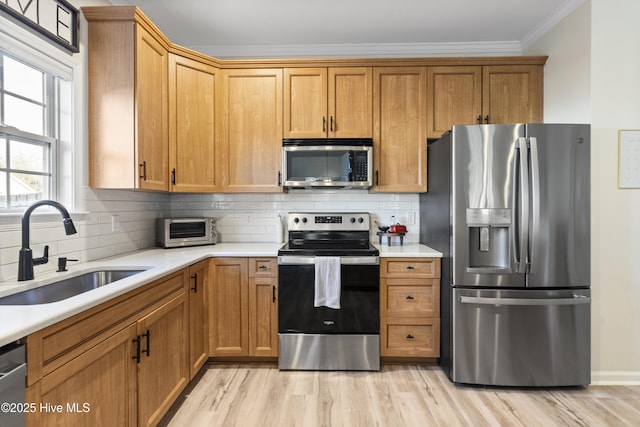 kitchen featuring tasteful backsplash, stainless steel appliances, light countertops, light wood-style floors, and a sink