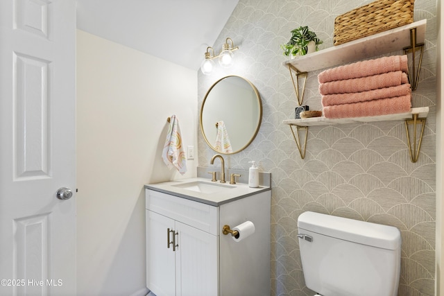 half bathroom featuring vanity, toilet, and wallpapered walls