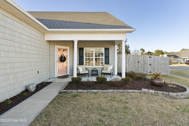 property entrance featuring covered porch, fence, a lawn, and roof with shingles