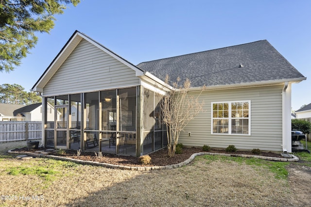 rear view of house with a sunroom, fence, a lawn, and roof with shingles