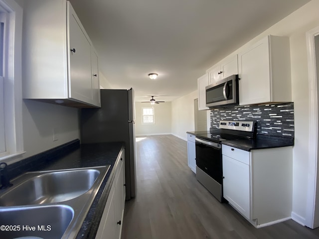 kitchen with stainless steel appliances, dark countertops, decorative backsplash, dark wood-type flooring, and a sink