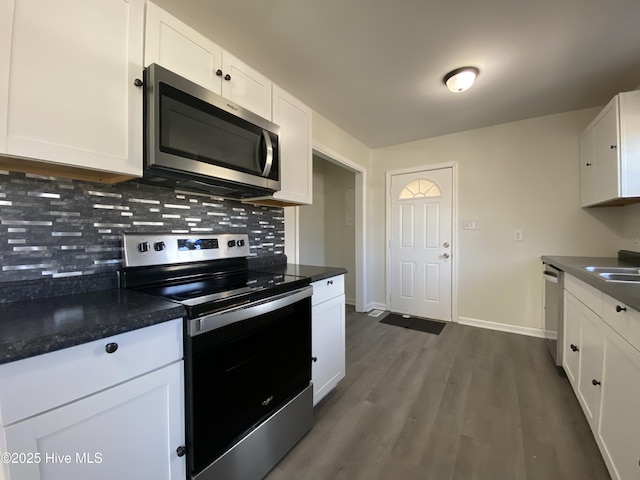 kitchen with stainless steel appliances, dark countertops, backsplash, and white cabinets