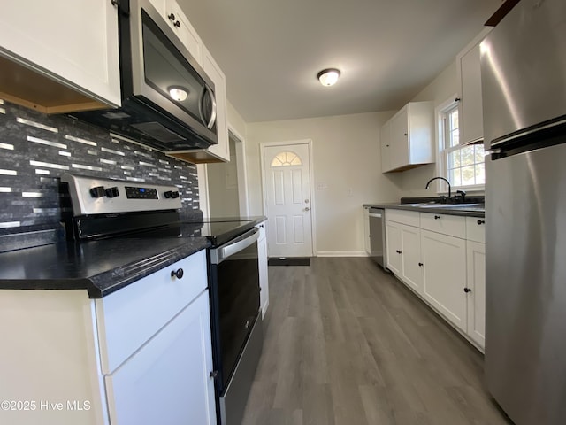 kitchen featuring stainless steel appliances, dark countertops, white cabinetry, and a sink