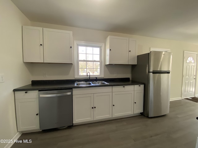 kitchen with stainless steel appliances, a sink, white cabinetry, dark wood-style floors, and dark countertops