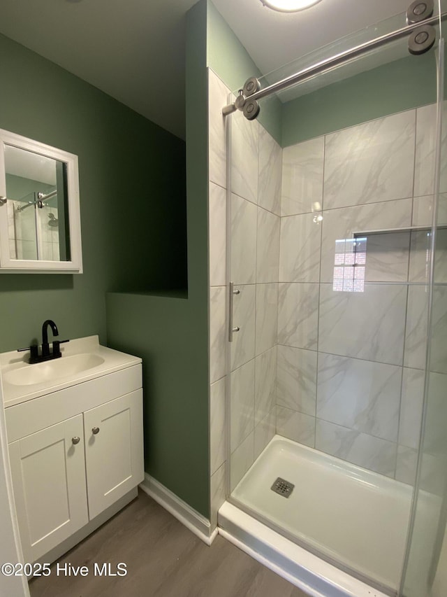 bathroom featuring wood finished floors, a shower stall, vanity, and baseboards