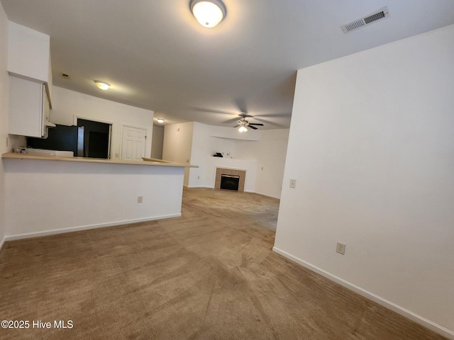 unfurnished living room featuring ceiling fan, a tile fireplace, light colored carpet, visible vents, and baseboards