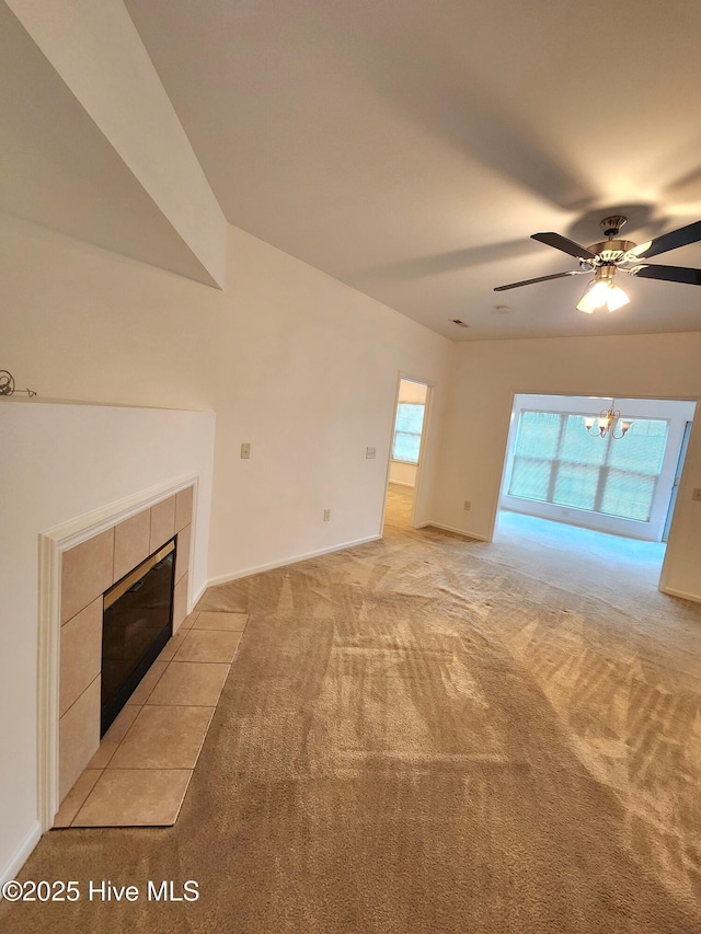 unfurnished living room featuring baseboards, light carpet, a tiled fireplace, and ceiling fan with notable chandelier