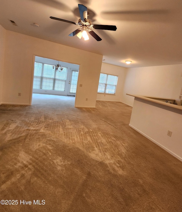 unfurnished living room with baseboards, visible vents, carpet flooring, and ceiling fan with notable chandelier