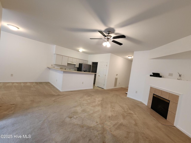 unfurnished living room with baseboards, light colored carpet, ceiling fan, and a tiled fireplace