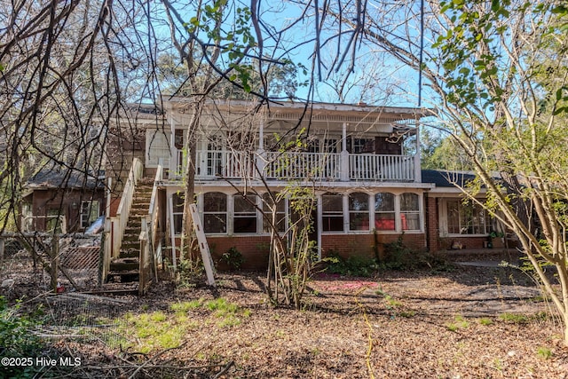 rear view of house with brick siding, a balcony, and stairs