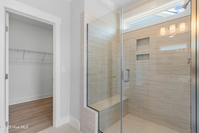 full bathroom featuring a spacious closet, wood finished floors, a shower stall, and baseboards