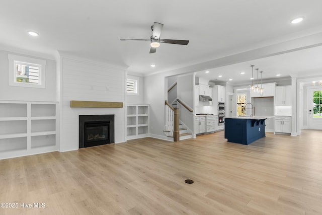 unfurnished living room with a large fireplace, a sink, light wood-style floors, ornamental molding, and stairway