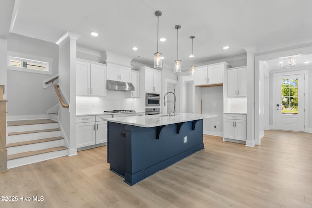 kitchen featuring under cabinet range hood, a sink, light wood-style floors, white cabinets, and backsplash