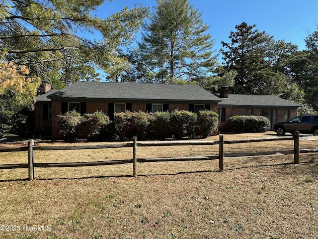 ranch-style house featuring a chimney, fence, a front lawn, and brick siding