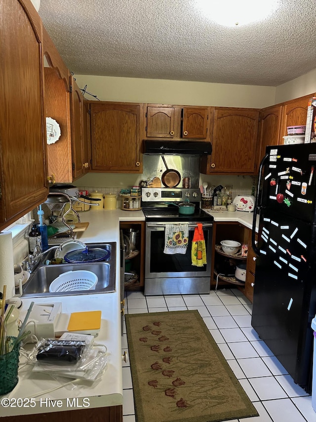 kitchen with light tile patterned floors, under cabinet range hood, light countertops, stainless steel electric range, and freestanding refrigerator