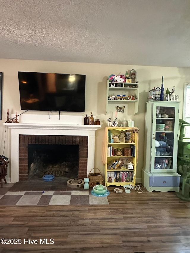 living area featuring a brick fireplace, a textured ceiling, and wood finished floors