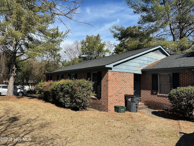 view of property exterior featuring brick siding, a lawn, and roof with shingles