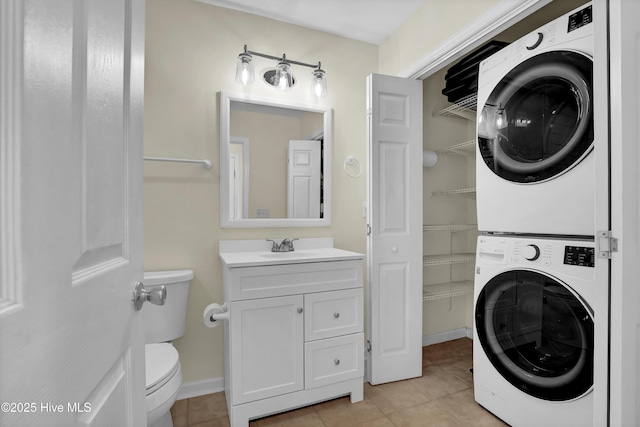 laundry area featuring stacked washer and clothes dryer, light tile patterned flooring, a sink, and baseboards