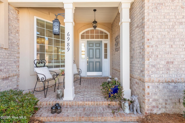 doorway to property featuring covered porch and brick siding