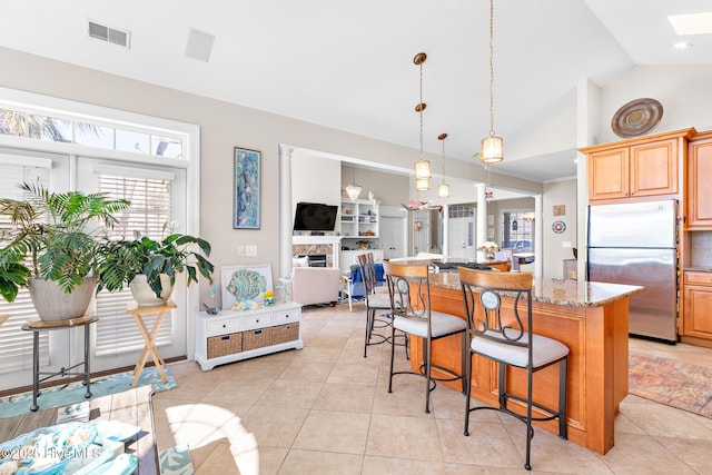 kitchen featuring light tile patterned floors, visible vents, a kitchen breakfast bar, freestanding refrigerator, and a center island