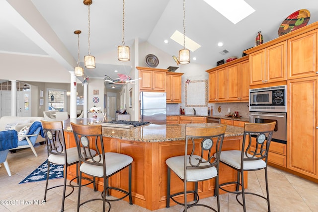 kitchen featuring a skylight, light tile patterned floors, open floor plan, light stone countertops, and stainless steel appliances