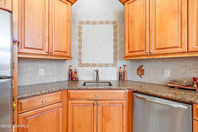 kitchen featuring appliances with stainless steel finishes, a sink, backsplash, and dark stone countertops