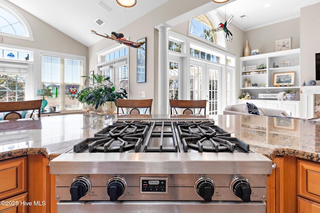 kitchen featuring brown cabinetry, light stone counters, french doors, ornate columns, and stainless steel range with gas cooktop