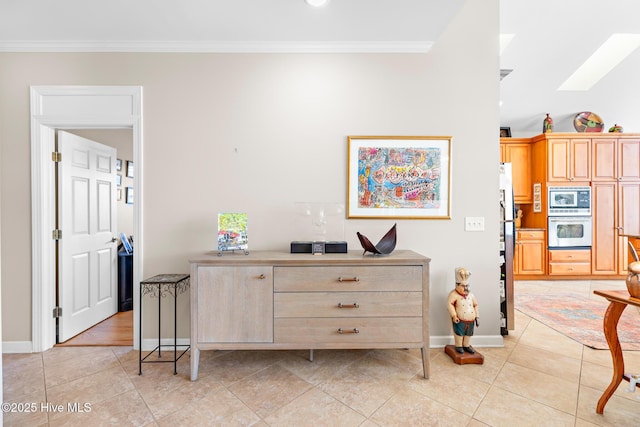 kitchen with a skylight, light tile patterned floors, baseboards, appliances with stainless steel finishes, and ornamental molding