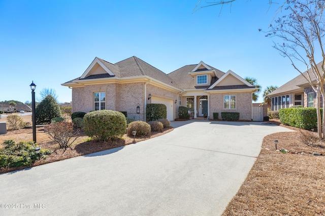 view of front facade featuring driveway, brick siding, an attached garage, and a gate