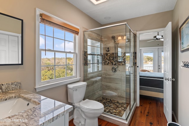 bathroom featuring toilet, ceiling fan, wood finished floors, vanity, and a shower stall