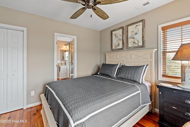 bedroom featuring baseboards, visible vents, ensuite bath, ceiling fan, and wood finished floors