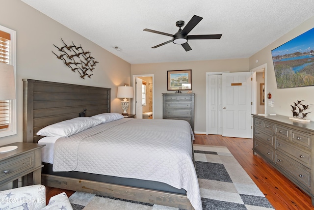 bedroom with visible vents, ceiling fan, wood finished floors, ensuite bathroom, and a textured ceiling