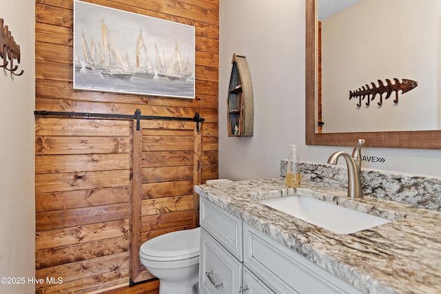 bathroom featuring toilet, wood walls, and vanity