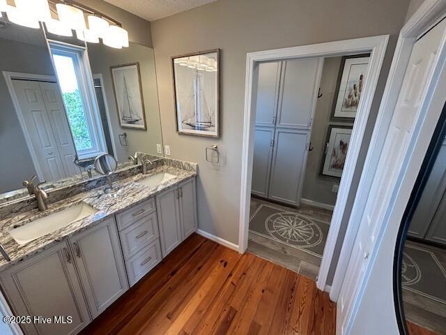 full bathroom with double vanity, a sink, baseboards, and wood finished floors