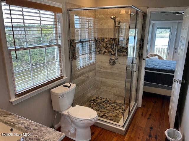 bathroom with a stall shower, wood finished floors, toilet, and a ceiling fan