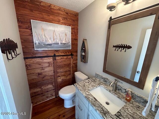 bathroom with wooden walls, toilet, wood finished floors, a textured ceiling, and vanity