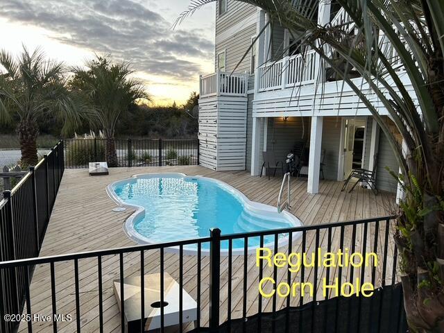 pool at dusk with a deck and a fenced in pool