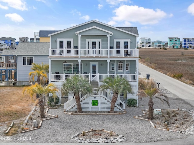 coastal inspired home featuring covered porch, french doors, stairs, and a balcony