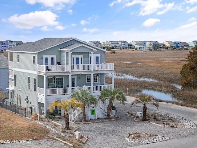 beach home with french doors, covered porch, a water view, a balcony, and stairs