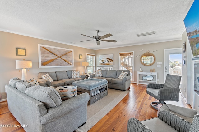 living area featuring light wood-type flooring, a healthy amount of sunlight, visible vents, and crown molding