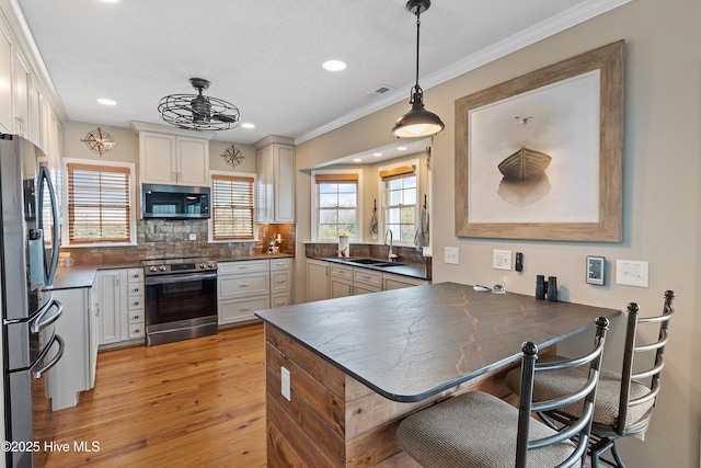 kitchen featuring visible vents, dark countertops, a peninsula, stainless steel appliances, and a sink