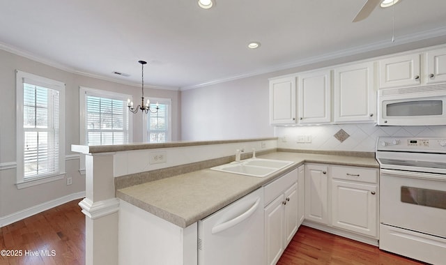 kitchen with white appliances, ornamental molding, a peninsula, a sink, and a wealth of natural light