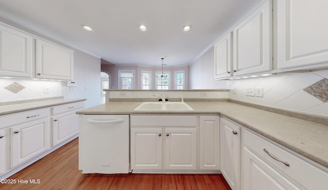 kitchen with a peninsula, white dishwasher, white cabinets, and a sink