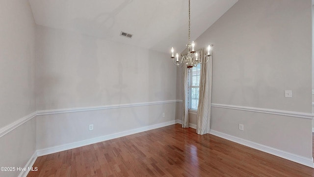 unfurnished room featuring lofted ceiling, a notable chandelier, wood finished floors, visible vents, and baseboards