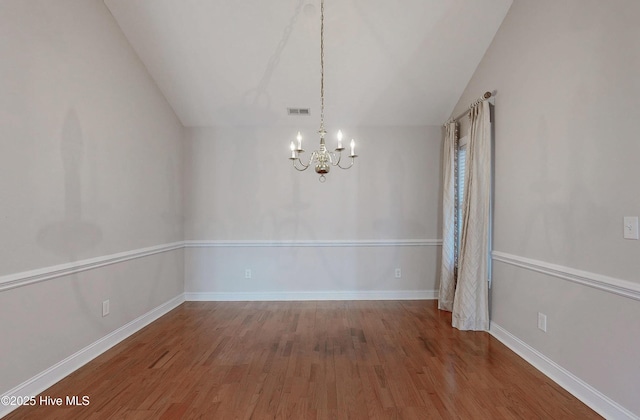 unfurnished dining area featuring baseboards, visible vents, lofted ceiling, wood finished floors, and a chandelier