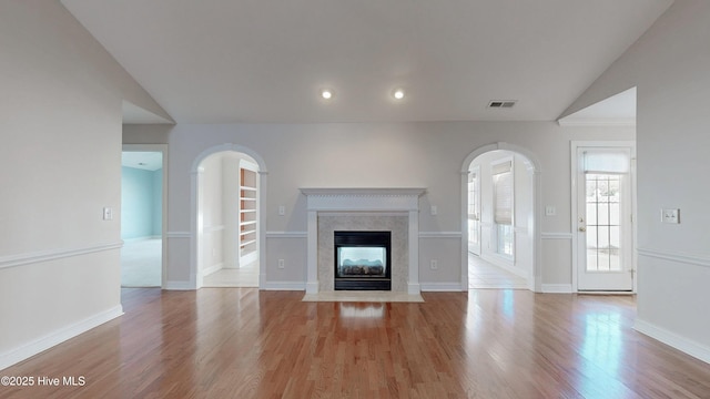 unfurnished living room with vaulted ceiling, a premium fireplace, and light wood-style flooring