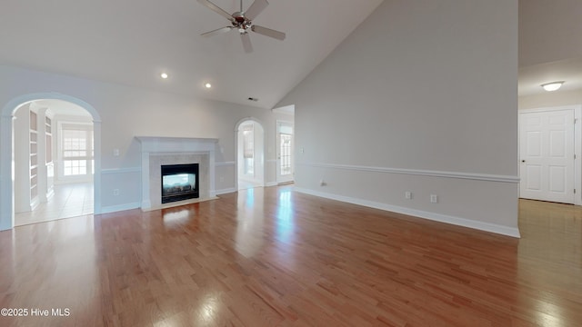 unfurnished living room featuring high vaulted ceiling, a premium fireplace, wood finished floors, a ceiling fan, and baseboards